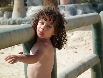 Portrait of shirtless boy standing by railing at beach