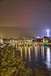 Illuminated buildings by river against sky in city at night