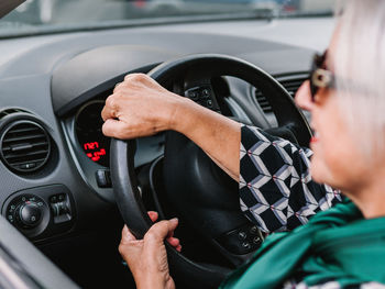 Cheerful senior female in elegant outfit driving modern shiny car in sunny day and looking away