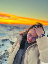 Side view of young woman standing against sky during sunset