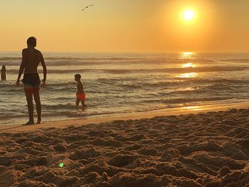 People on beach against sky during sunset