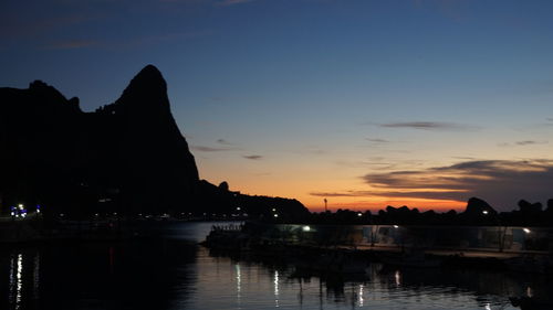 River by illuminated city against sky at sunset