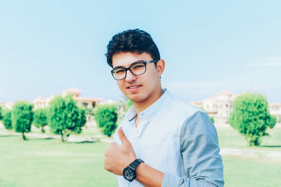 Portrait of man showing thumbs up sign while standing on field against sky