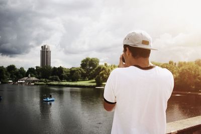 Rear view of man photographing building and river against cloudy sky