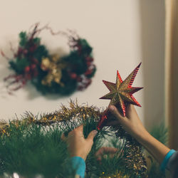 Cropped image person fixing tree topper on christmas tree at home