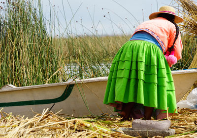 Rear view of woman bending by boat on field