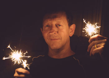 Portrait of man holding sparkler at night