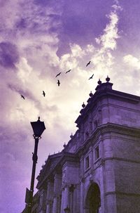 Low angle view of birds flying against dramatic sky