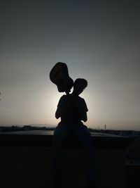 Silhouette man holding guitar while standing against clear sky during sunset