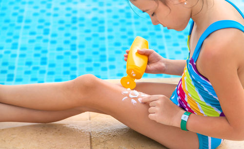 Midsection of girl applying suntan lotion by swimming pool