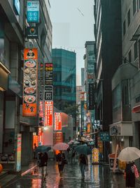 People walking on wet street amidst buildings in city