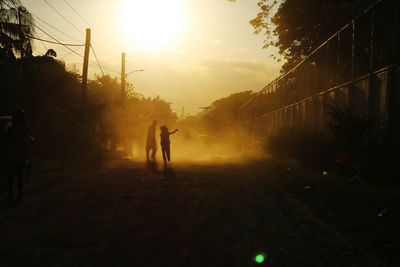 Silhouette people on road against sky during sunset