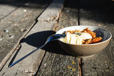 A bowl of apple crumble with ice-cream over a wooden table. 