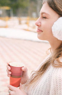 Teenager girl  holding coffee to go. girl in white earmuffs drinking take away drink. 