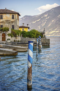 Wooden post in river by buildings against sky