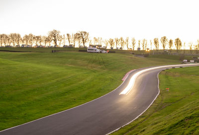 Scenic view of road amidst field against clear sky