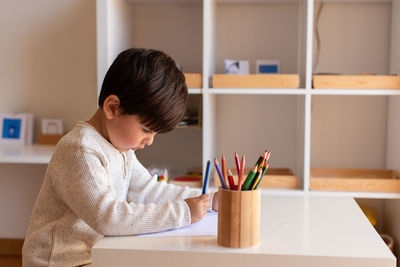 Side view of boy drawing on paper while sitting at home