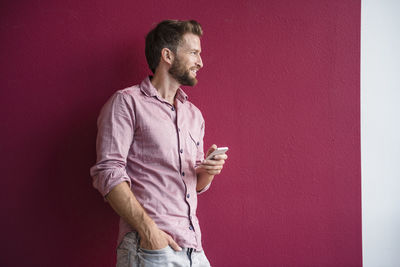 Man standing against purple wall holding cell phone