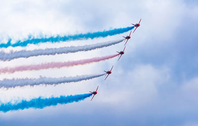 Low angle view of fighter plane performing smoking stunt against cloudy sky