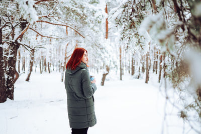 Cheerful girl in warm clothes playing with snow outdoors near the beautiful forest