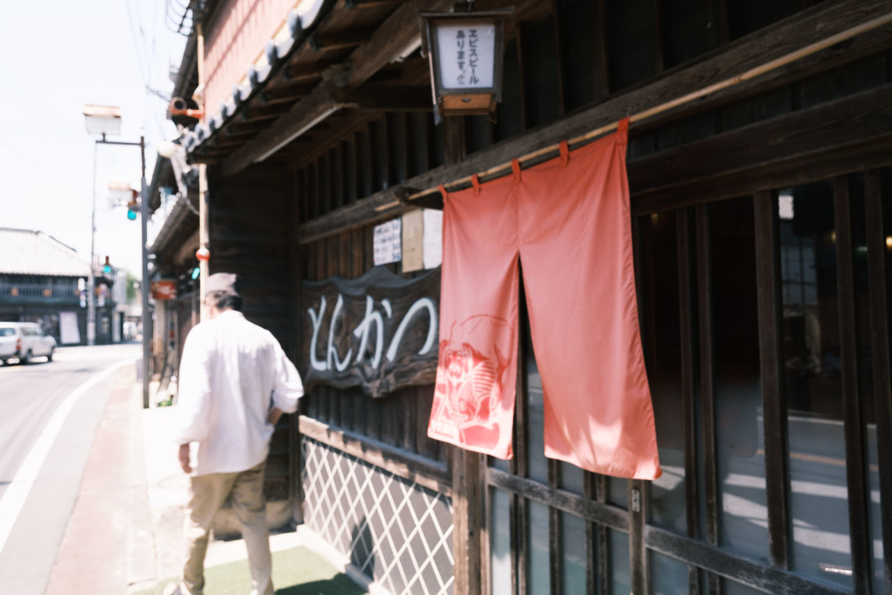 REAR VIEW OF PEOPLE WALKING ON STREET BY BUILDING