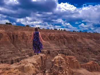 Rear view of woman standing on rock formation against sky