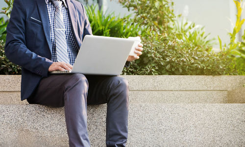 Rear view of man using mobile phone while sitting on plant