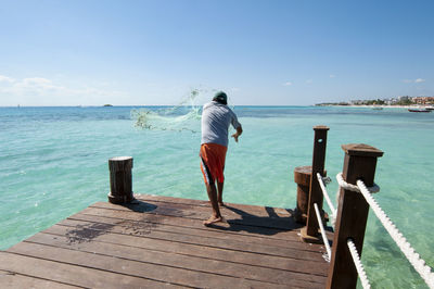 Rear view of man standing on pier over sea against sky