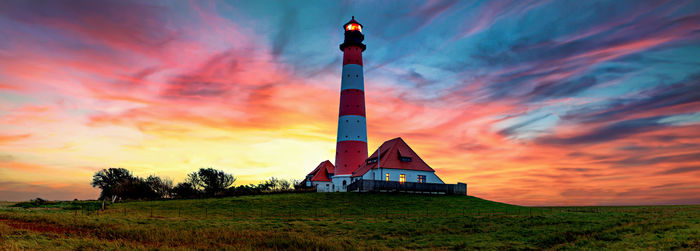 Lighthouse on field against sky during sunset