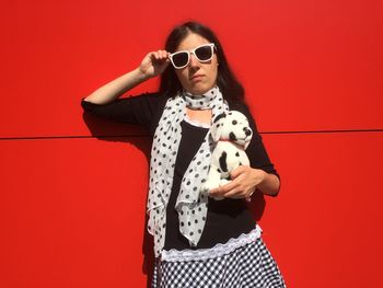 Portrait of young woman with toy dog against red wall