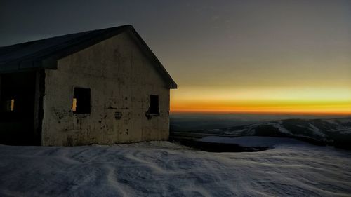 Building on snow covered land against sky during sunset