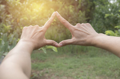 Cropped hands of woman forming shape against trees