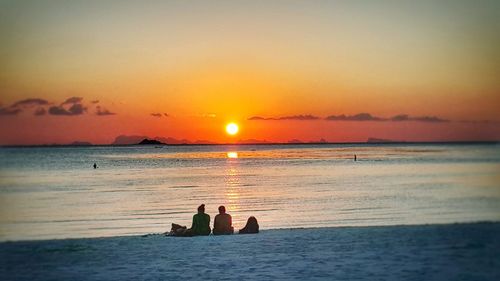 Silhouette men in sea against romantic sky at sunset