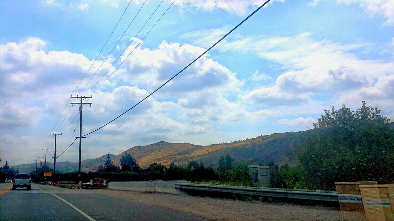 power line, sky, transportation, electricity pylon, cable, road, cloud - sky, connection, tree, mountain, electricity, car, cloud, power supply, mode of transport, street, land vehicle, cloudy, power cable, the way forward