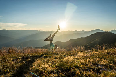 Woman doing handstand on mountain against sky during sunset