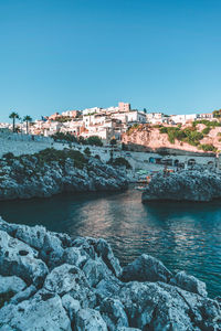 Buildings by sea against clear blue sky