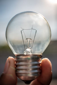 Hand holding light bulb against sky