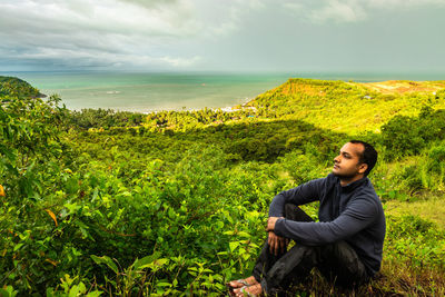 Full length of man looking away while sitting outdoors