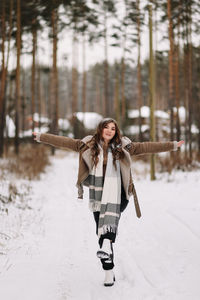 A funny pretty curly-haired girl in winter clothes is having fun walking alone in a snowy forest