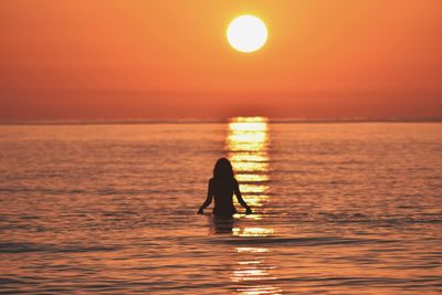 Silhouette woman in sea against sky during sunset