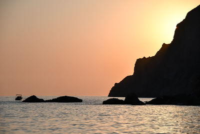 Silhouette rocks on sea against sky during sunset