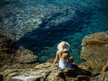 Rear view of woman standing on rock by sea