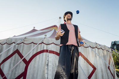 Male artist juggling balls while standing in front of circus tent