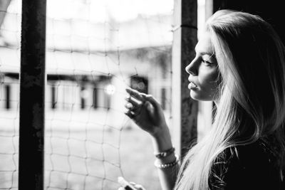 Side view of young woman standing by window