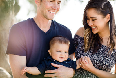 Parents sitting under tree smiling at infant son