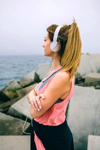 Side view of young woman standing by sea against sky