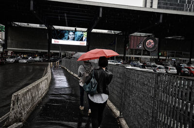 Rear view of woman walking on wet road during rainy season