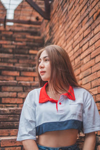 Beautiful young woman standing against brick wall