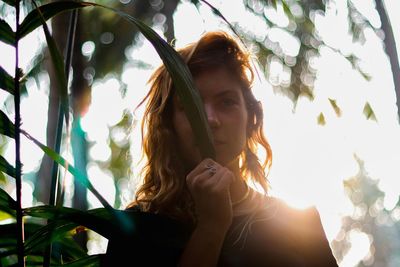 Low angle portrait of woman against tree