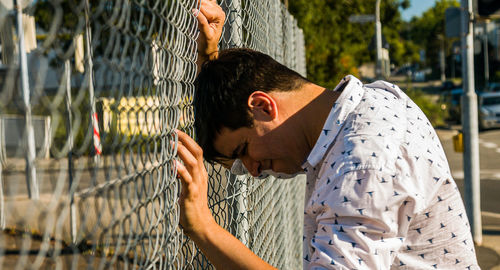 Distraught man crying and pushing head against fence. profile view.